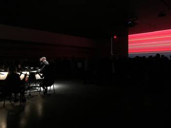 An orchestra plays in front of a crowd that sits in the dark